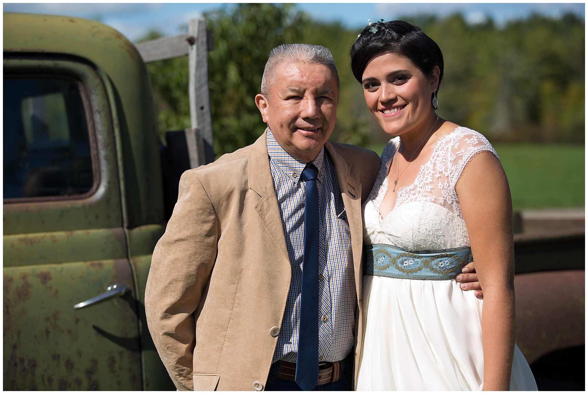 A bride and her dad standing in front of an old truck