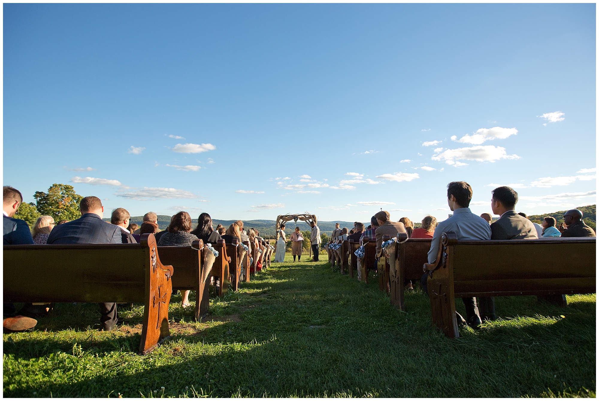 Wide angle photo of the wedding ceremony beginning with bright sunshine and blue skies with a few distant clouds.