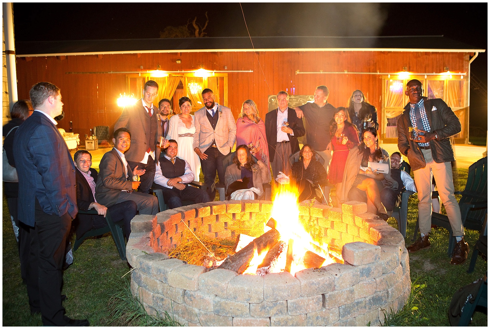 Photo of wedding party and friends around a fire pit outside of the wedding reception barn.