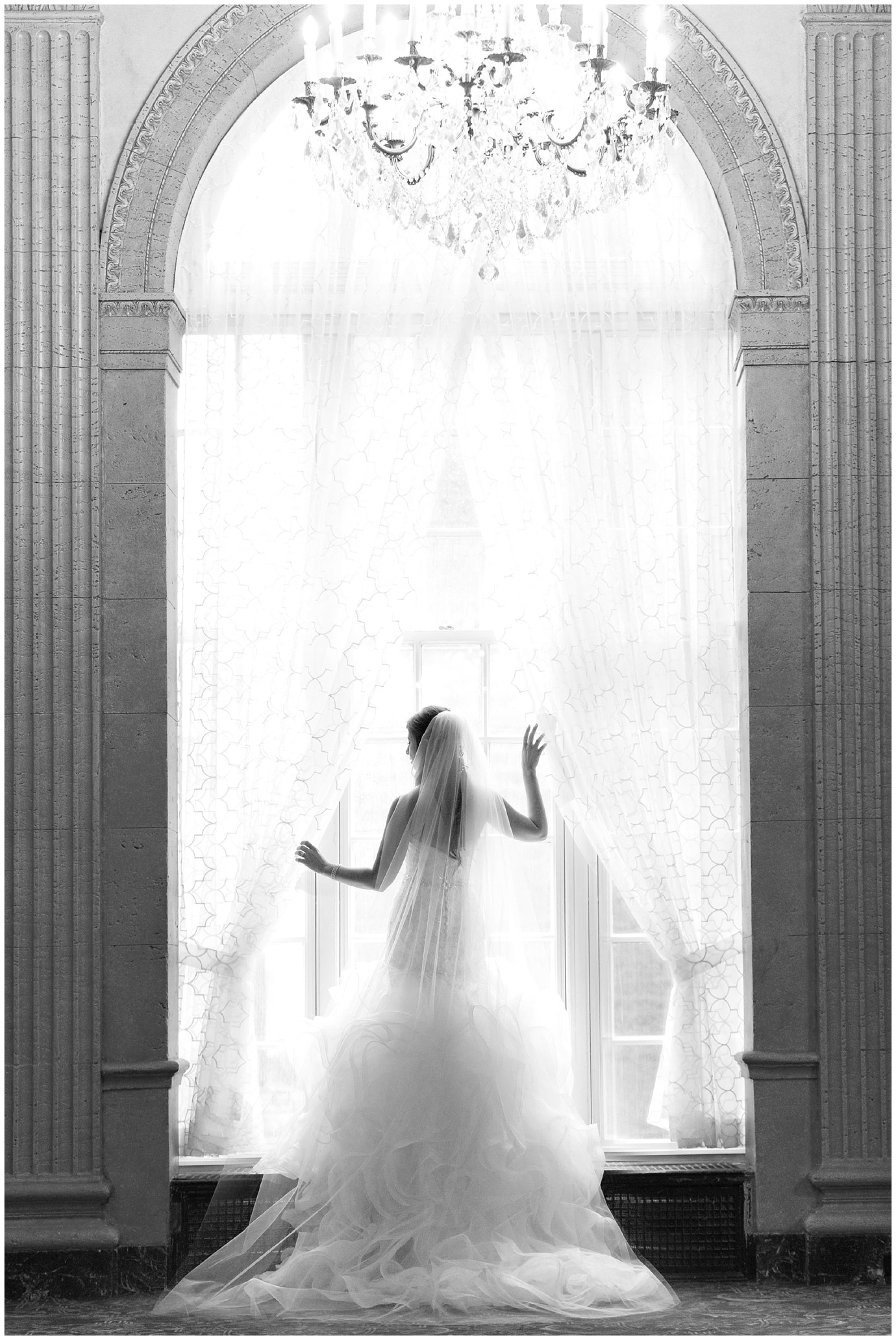 A portrait of a bride semi silhouetted and framed by a large arched window.
