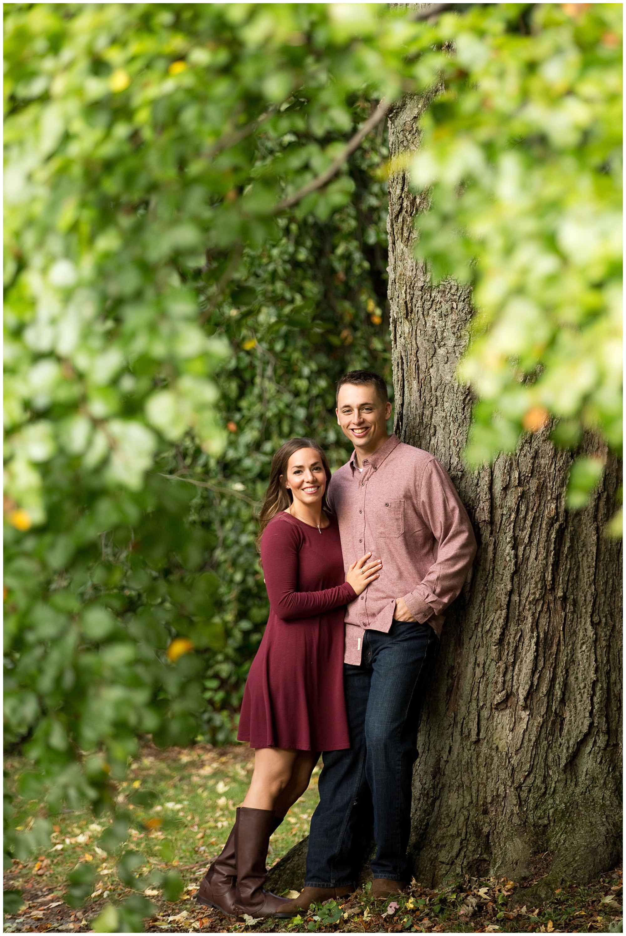 Photo of an engaged couple smiling at the camerea under a tree.