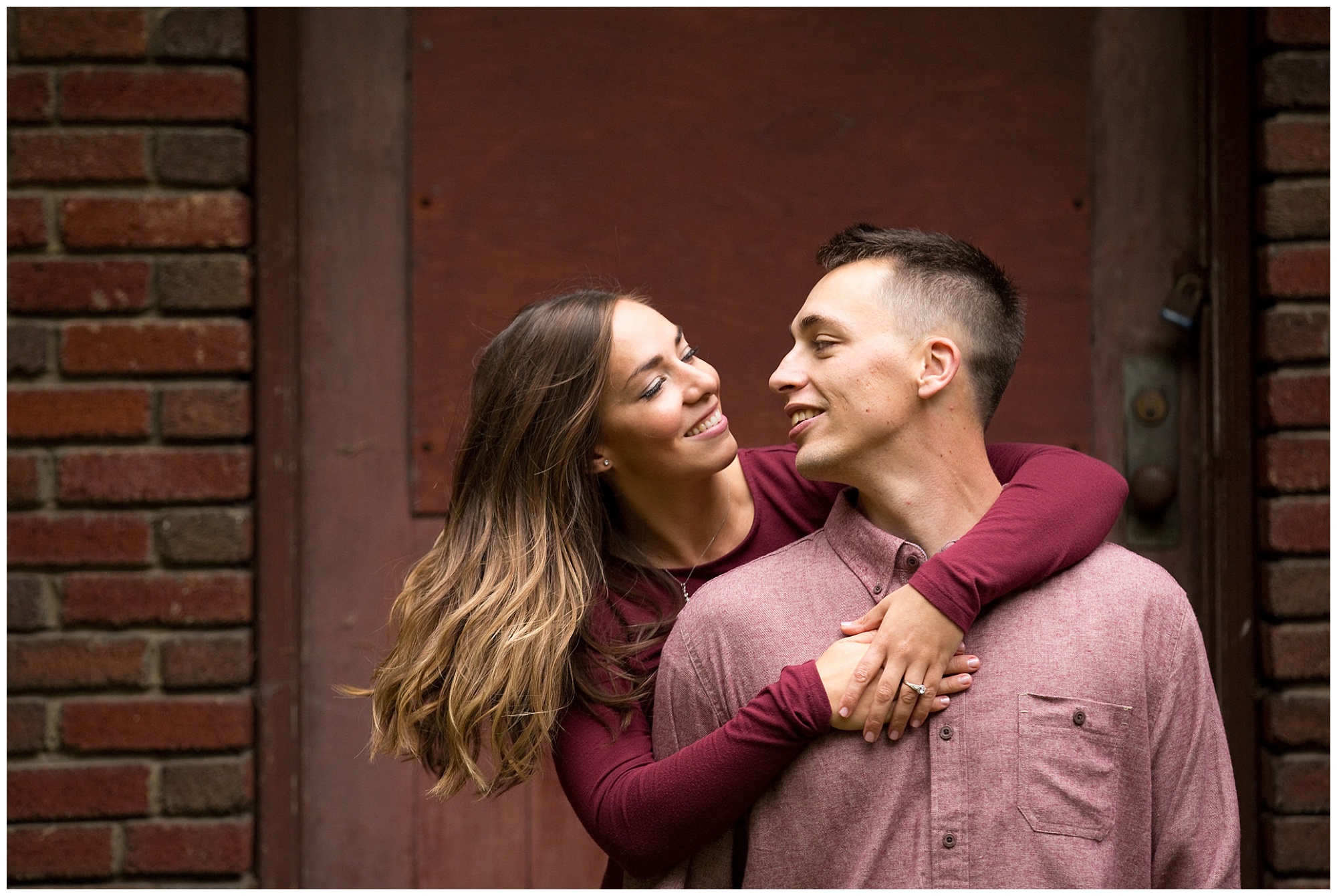 Photo of an engaged couple with her arms wrapped around him from behind.