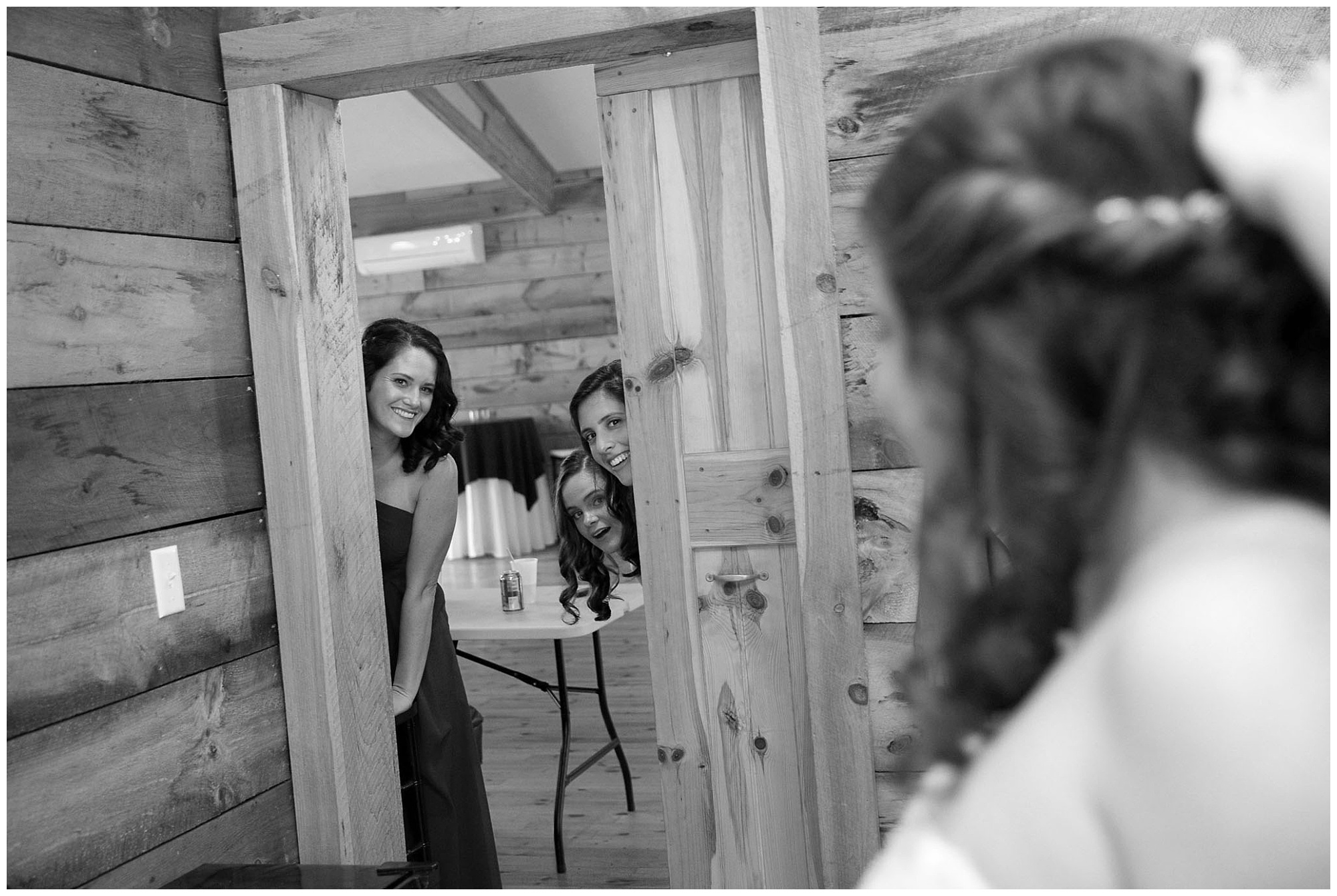 Photo of a bride in the foreground looking at her bridesmaid peek at her through the room door.