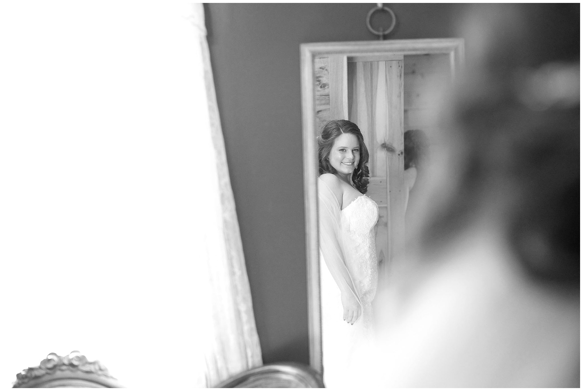 A lovely bride giving herself a smiling once over in her fully doned wedding dreess while looking in a mirror