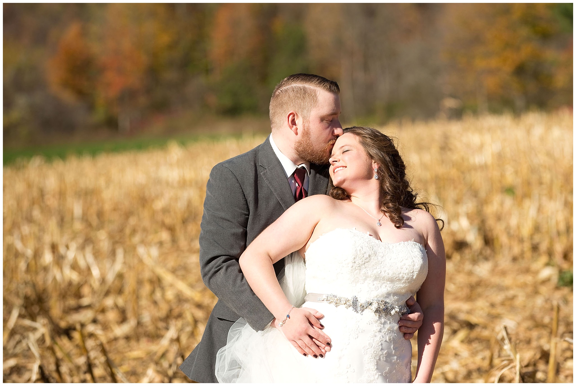 A portrait photo of a bride and groom, he kissing her forehead while she smiles with her eyes closed.