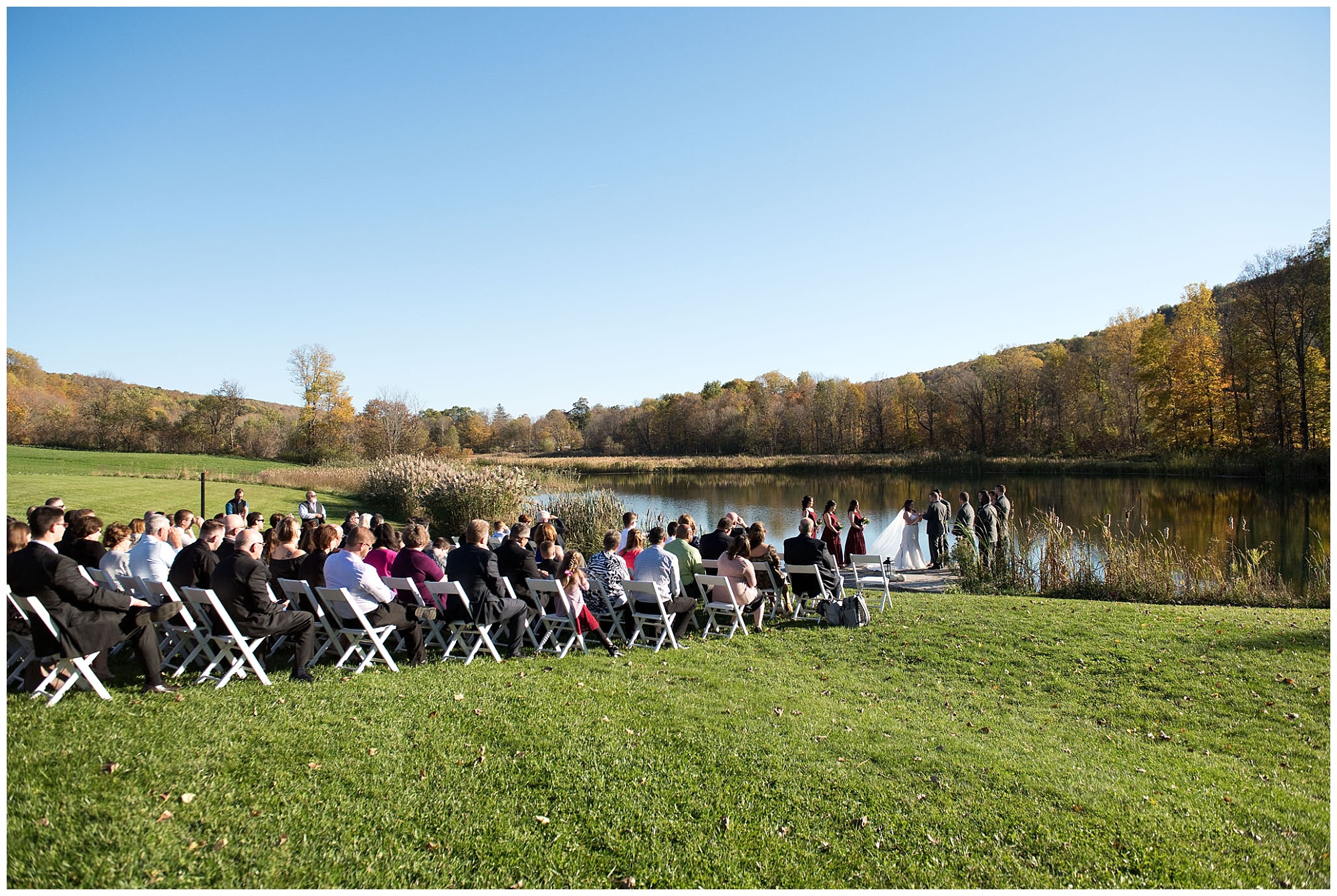 I wide angle view of the pondside wedding ceremony with view of the guests and wedding party.