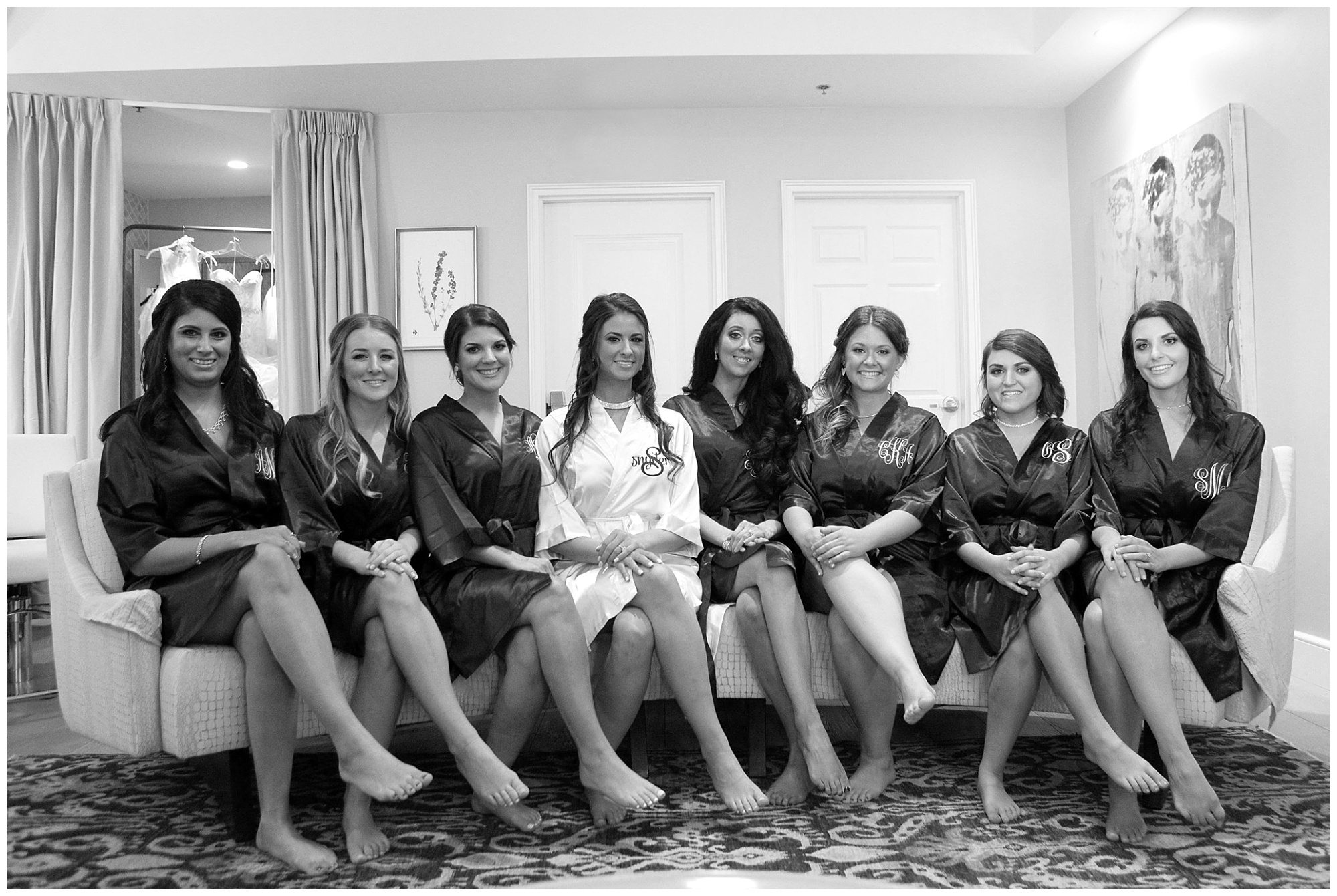 Photo of a bride and her bridesmaids sitting cross legged on th e bridal suite couch.